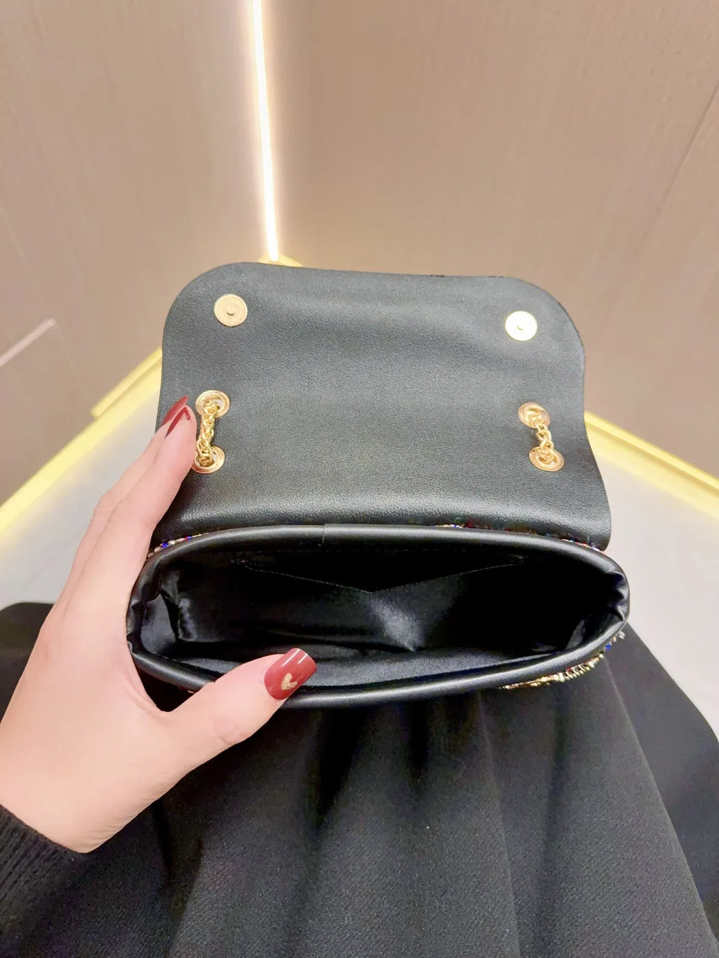 A hand holds an elegant dark gray leather clutch bag with gold hardware against a light background.