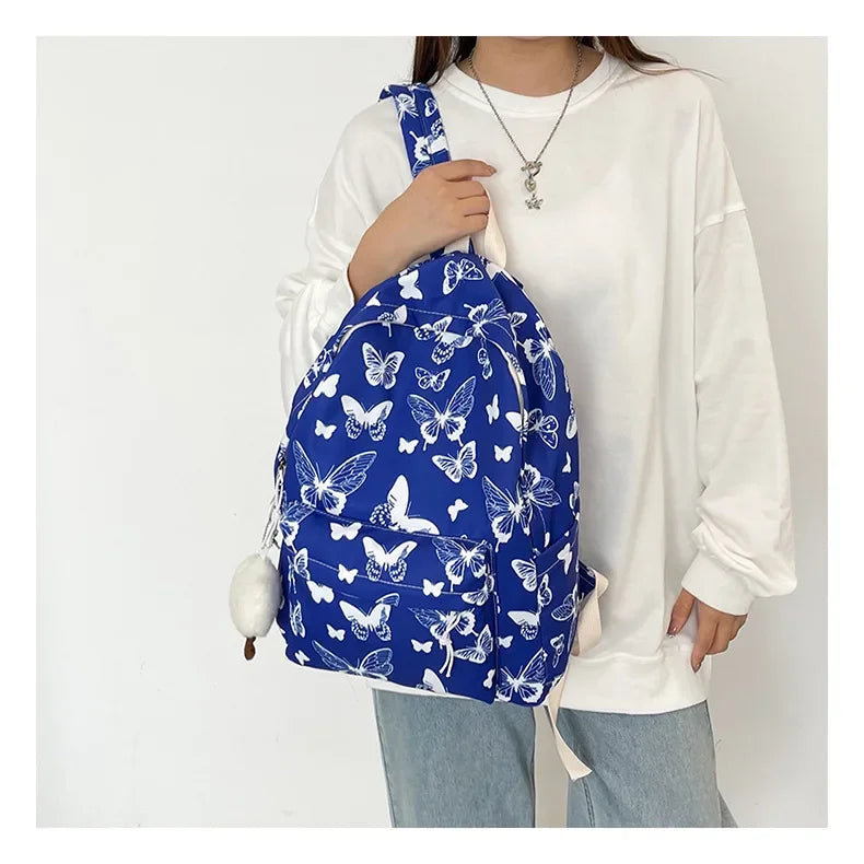 A woman is holding a blue butterfly patterned backpack against a white shirt and jeans.