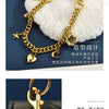 Gold chain necklace with a flower pendant displayed on a white fluffy background and next to a black bag.