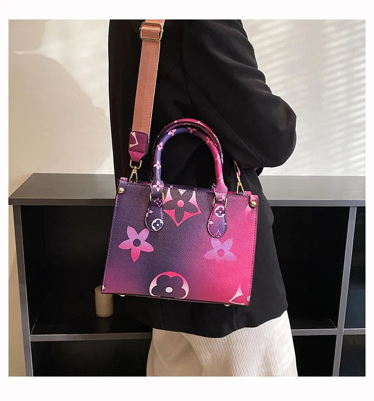 A woman holds a pink and purple patterned ladies' shoulder tote bag with a tan strap against a dark background.