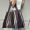 A person is holding a dark brown and beige striped foldable oxford grocery tote bag against a gray wall.