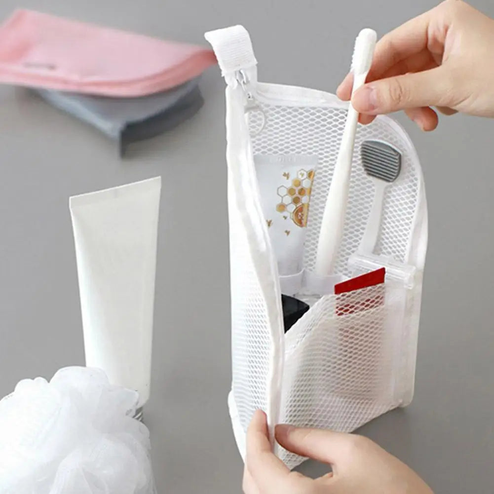 Una mano coloca un cepillo de dientes blanco y un pequeño artículo cosmético en una bolsa de viaje de malla transparente.