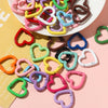 A collection of heart-shaped metal spring clasps in various colors and finishes arranged on a white plate.