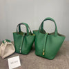 A dark green genuine leather bucket bag with a strap is displayed on a gray surface next to a name tag.