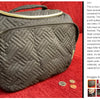 A dark quilted cosmetic organizer bag with a gold zipper and handle resting on a red fabric surface.