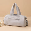 A light gray Oxford gym duffel bag with padded straps resting on a beige surface.