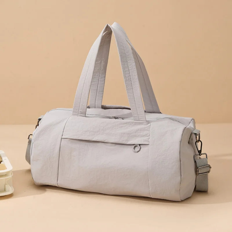 A light gray Oxford gym duffel bag with padded straps resting on a beige surface.