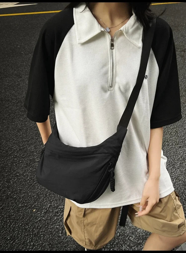 A person is wearing a black short-sleeved shirt over a white polo and carrying a black nylon crossbody bag.
