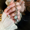 A hand holds an ocean pearl charm bracelet featuring starfish, shell, and pearl accents.