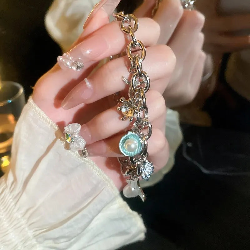 A hand holds an ocean pearl charm bracelet featuring starfish, shell, and pearl accents.