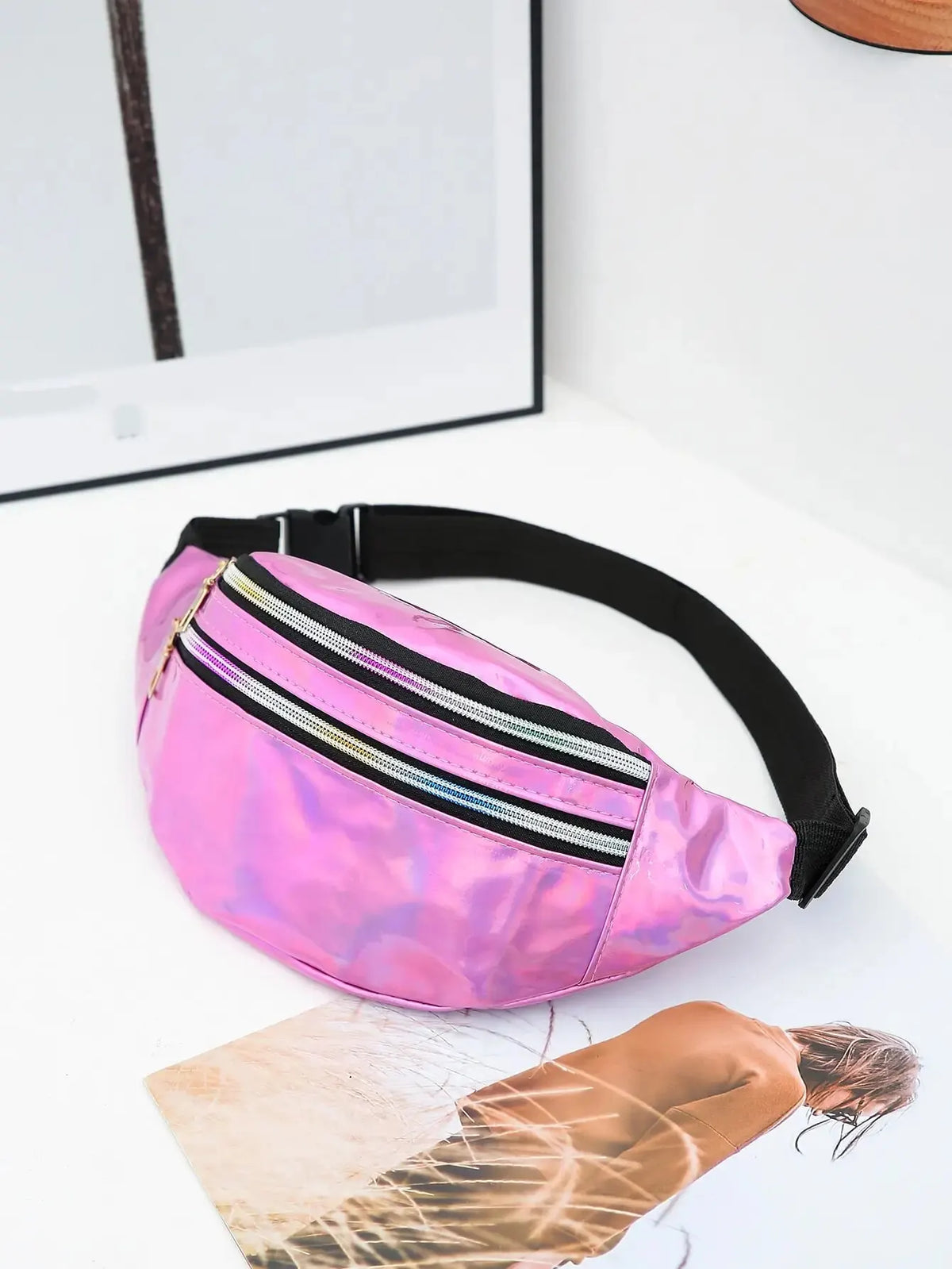 A pink holographic sequin waist bag with a black adjustable strap resting on a white surface.
