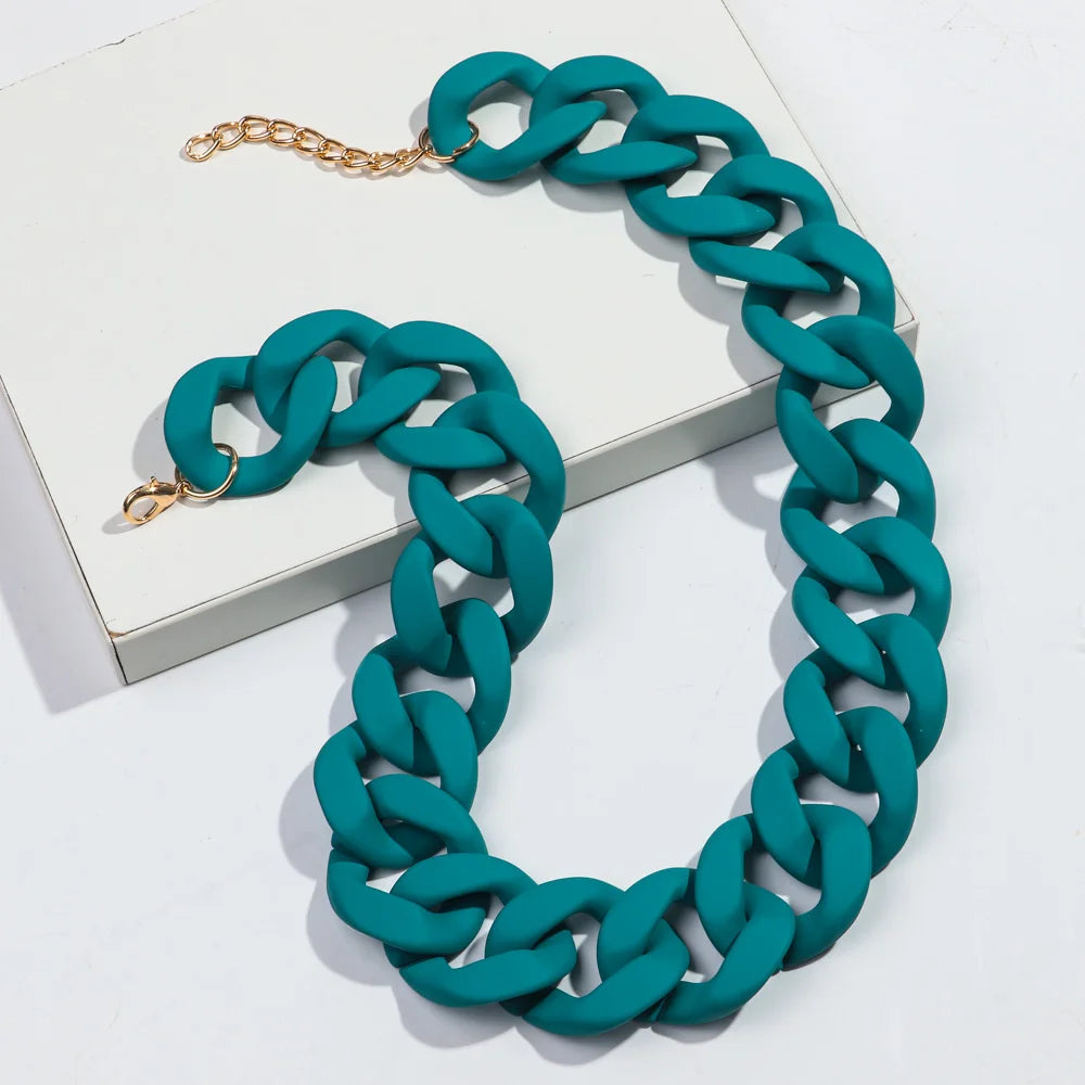 A teal matte acrylic chain necklace with a gold clasp is displayed on a white surface.