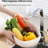 A hand is placing various colorful vegetables like carrots, corn, and bell peppers into a white plastic drain and storage bas