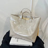 Bolso de PVC beige minimalista con asas marrón claro sobre una superficie oscura.