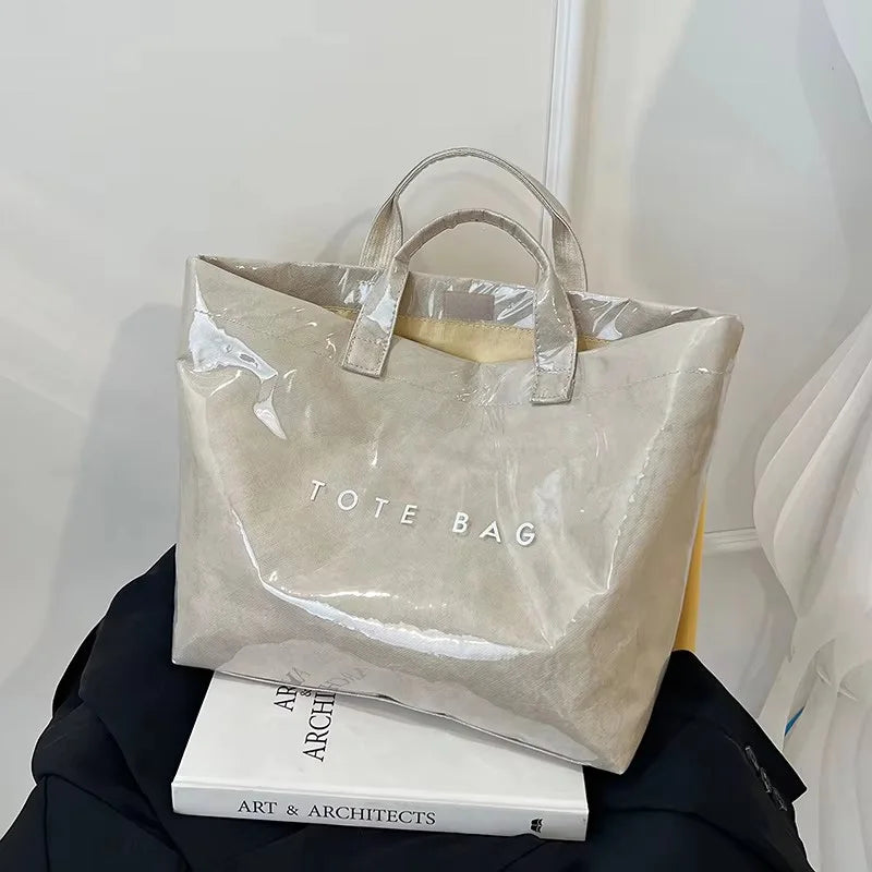Bolso de PVC beige minimalista con asas marrón claro sobre una superficie oscura.