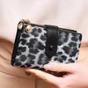 A close-up of a black and white leopard print women's wallet with gold hardware being held by a hand.