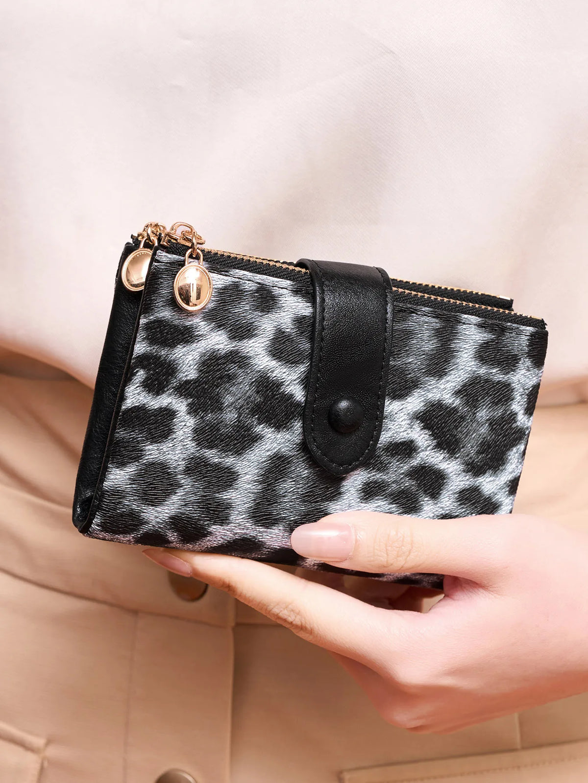 A close-up of a black and white leopard print women's wallet with gold hardware being held by a hand.