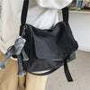 Una bolsa cruz estilo lienzo negra con un dije de peluche gris, usada por una persona.
