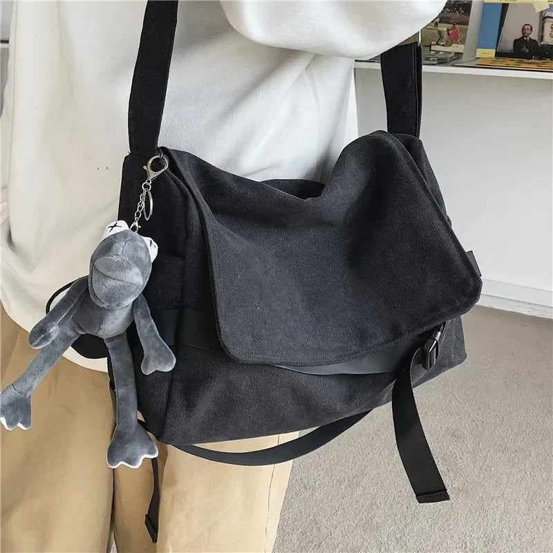 Una bolsa cruz estilo lienzo negra con un dije de peluche gris, usada por una persona.