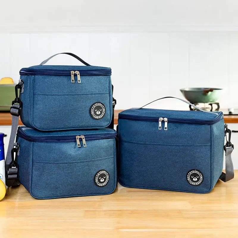 A navy blue insulated portable lunch bag with a shoulder strap is shown on a wooden surface.