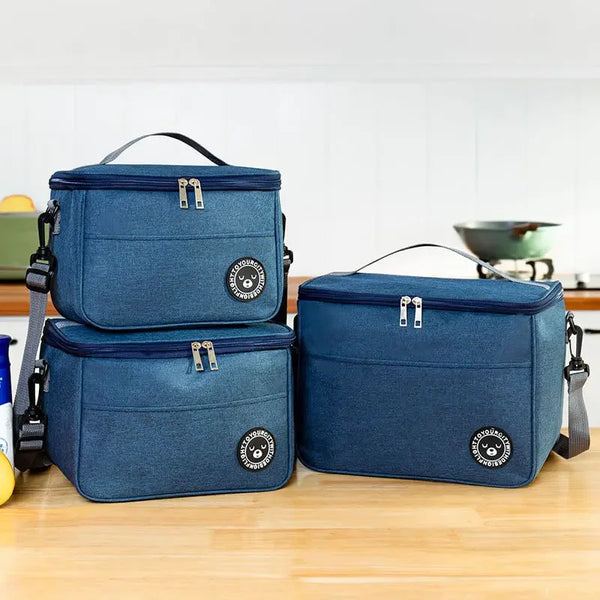 A navy blue insulated portable lunch bag with a shoulder strap is shown on a wooden surface.