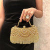 A hand holds an elegant diamond rhinestone evening clutch bag with a golden tassel against a black dress.