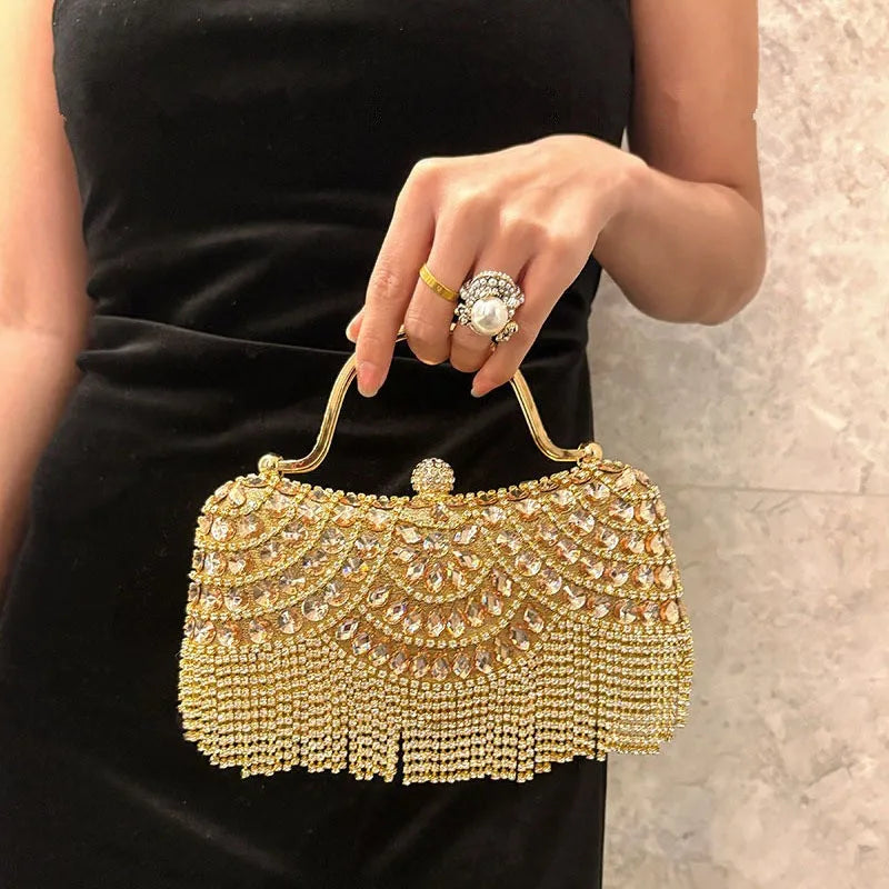A hand holds an elegant diamond rhinestone evening clutch bag with a golden tassel against a black dress.
