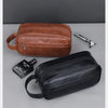 A brown leather travel cosmetic bag next to a black leather bag and a silver metal object.