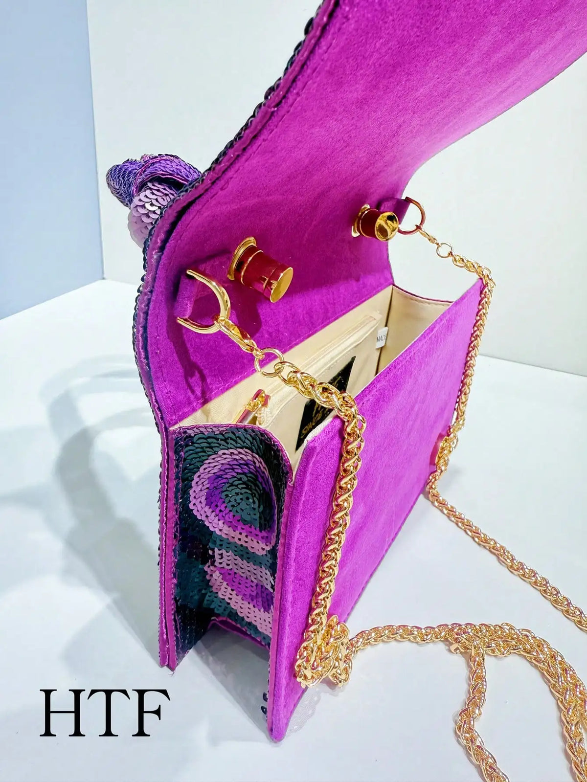 A vibrant magenta clutch bag featuring purple sequins and gold chain detailing.
