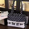 A black tote bag featuring white polka dots, piano key accents, and lace trim, displayed on a dark surface.