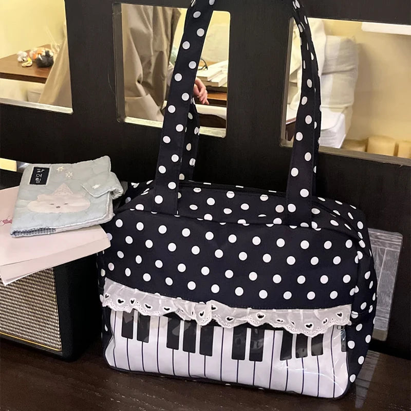 A black tote bag featuring white polka dots, piano key accents, and lace trim, displayed on a dark surface.