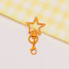 A small, gold-toned metal keychain clasp set shaped like a star and a ring, resting on a yellow checkered cloth.
