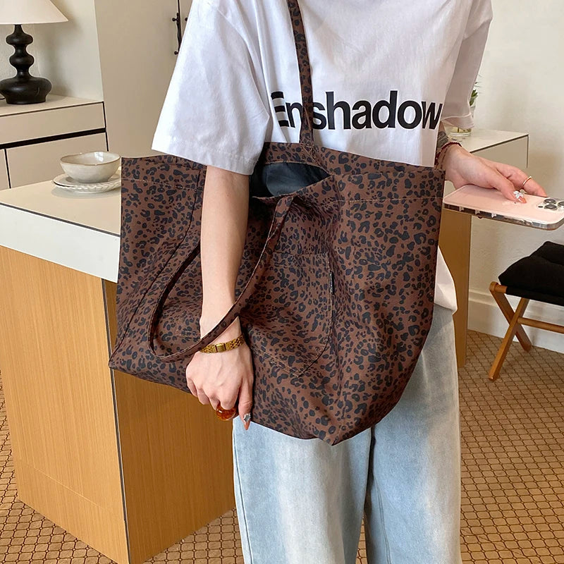 A person wearing a white t-shirt and light jeans holds a brown leopard print canvas tote bag.