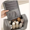 A gray waterproof hanging toiletry bag is open, displaying various skincare and cosmetic products inside.