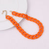 Orange braided acrylic statement choker necklace with gold-tone clasps displayed on a white plate.