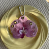 A realistic purple orchid flower is displayed on a yellow plate, attached to a silver keychain.