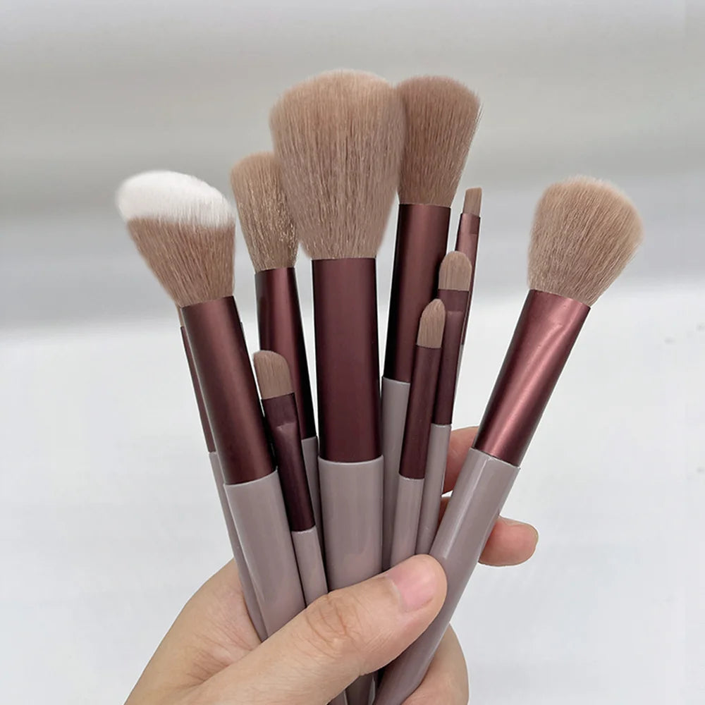 Una mano sostiene un juego de trece pinceles de maquillaje profesionales con cerdas de tonos marrones y beige y mango metálic