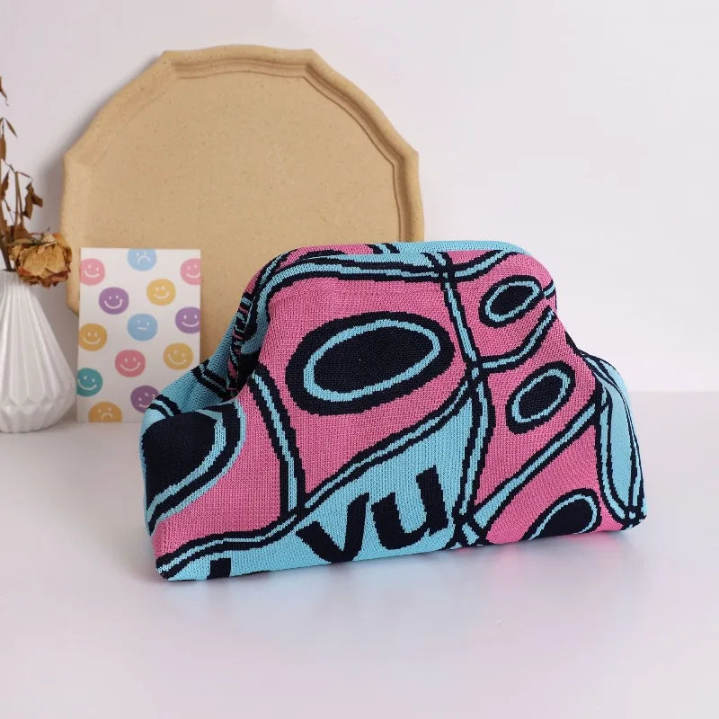 A pink and blue knitted clip bag with an abstract pattern is displayed on a white surface next to a beige object.