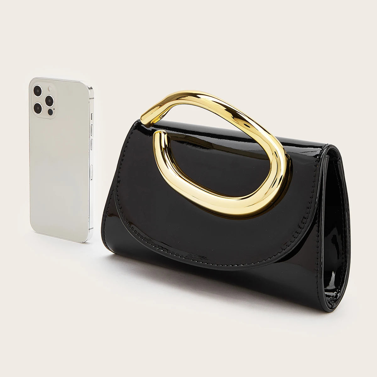 A black elegant women's clutch purse with a gold-toned handle next to a white smartphone.