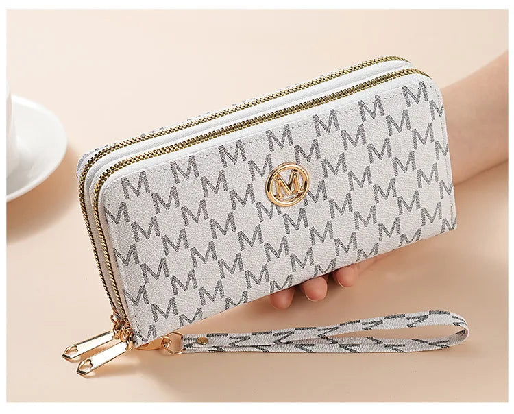 A light gray patterned double zipper wallet with a gold monogram and a leather strap.