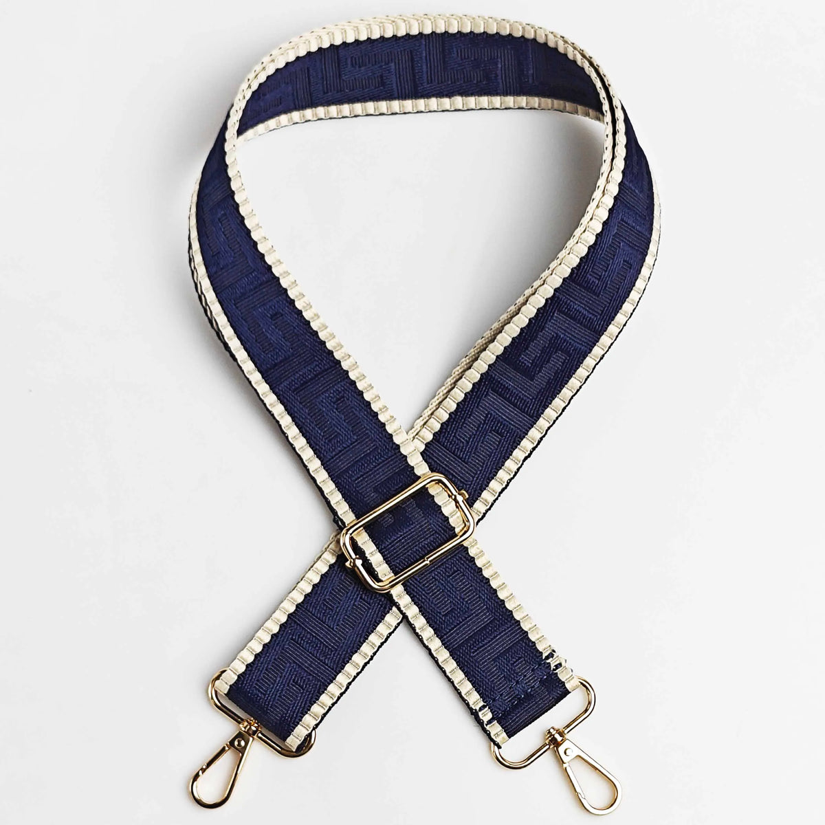 A navy blue and beige patterned adjustable crossbody bag strap with a gold buckle.
