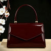 A glossy burgundy evening handbag with a leather strap and gold hardware resting on a light wooden surface.