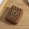 A brown leopard print double zipper wallet resting on a light wooden surface.