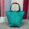 A teal leather bucket bag with a dark green strap is displayed against a backdrop of various colored fabric.