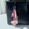 A pink heart keychain with a braided rope is hanging from a black leather tote bag.