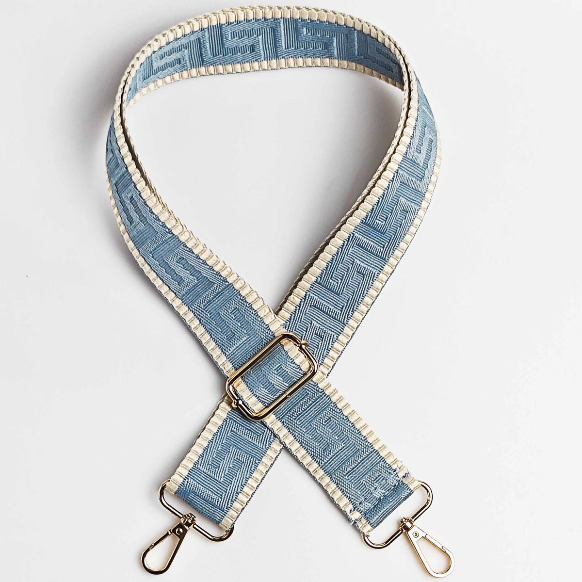 A light blue and beige patterned adjustable crossbody bag strap with a gold buckle.