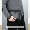 A close-up of a man wearing a grey sweater and black pants, holding a black PU leather business casual handbag.