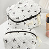 White quilted makeup bag with black trim and ribbon detail resting on a white surface.