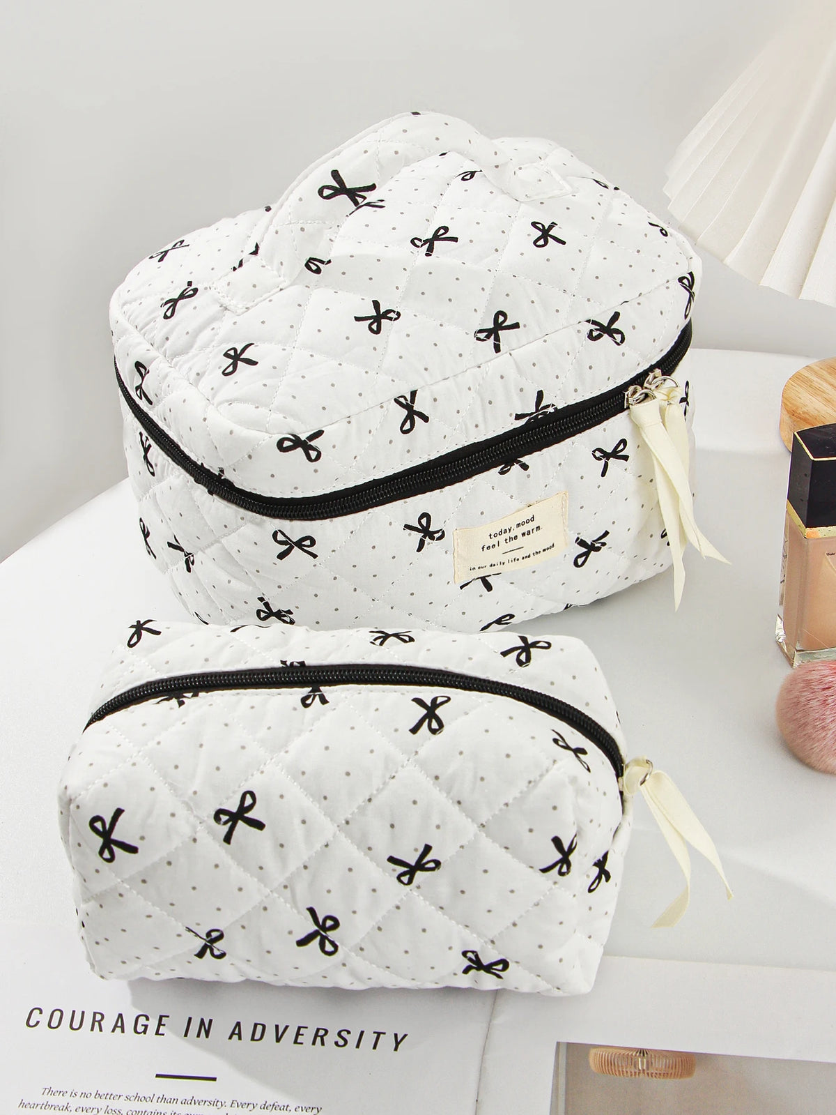 White quilted makeup bag with black trim and ribbon detail resting on a white surface.