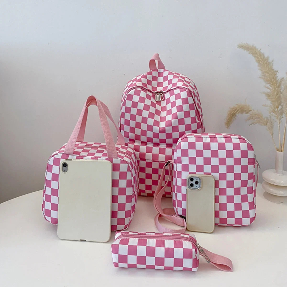 A pink and white checkerboard multi-pocket backpack with a matching pouch and a small wallet on a white surface.